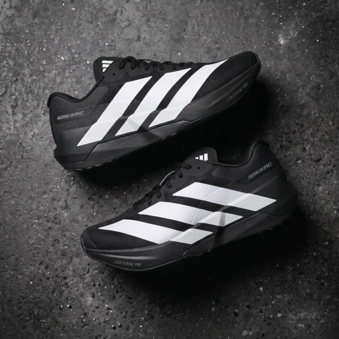A pair of Adidas Dropset shoes in black and white, arranged diagonally on a dark, textured concrete surface.