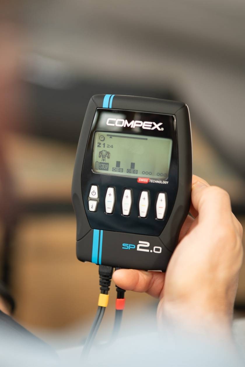 A woman using the Compex SP 2.0 EMS muscle stimulator for a muscle strengthening session