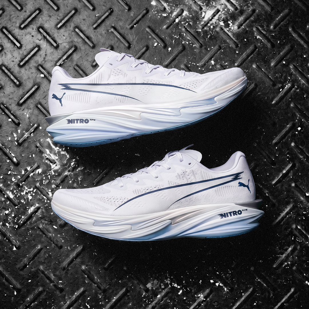 A pair of Puma Nitro running shoes in white with navy blue accents, displayed on a textured black diamond plate background.