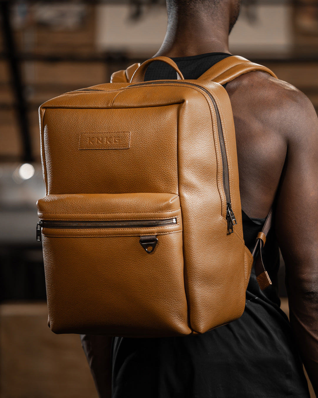 Man wearing tan leather KNKG HERITAGE Backpack inside boxing gym