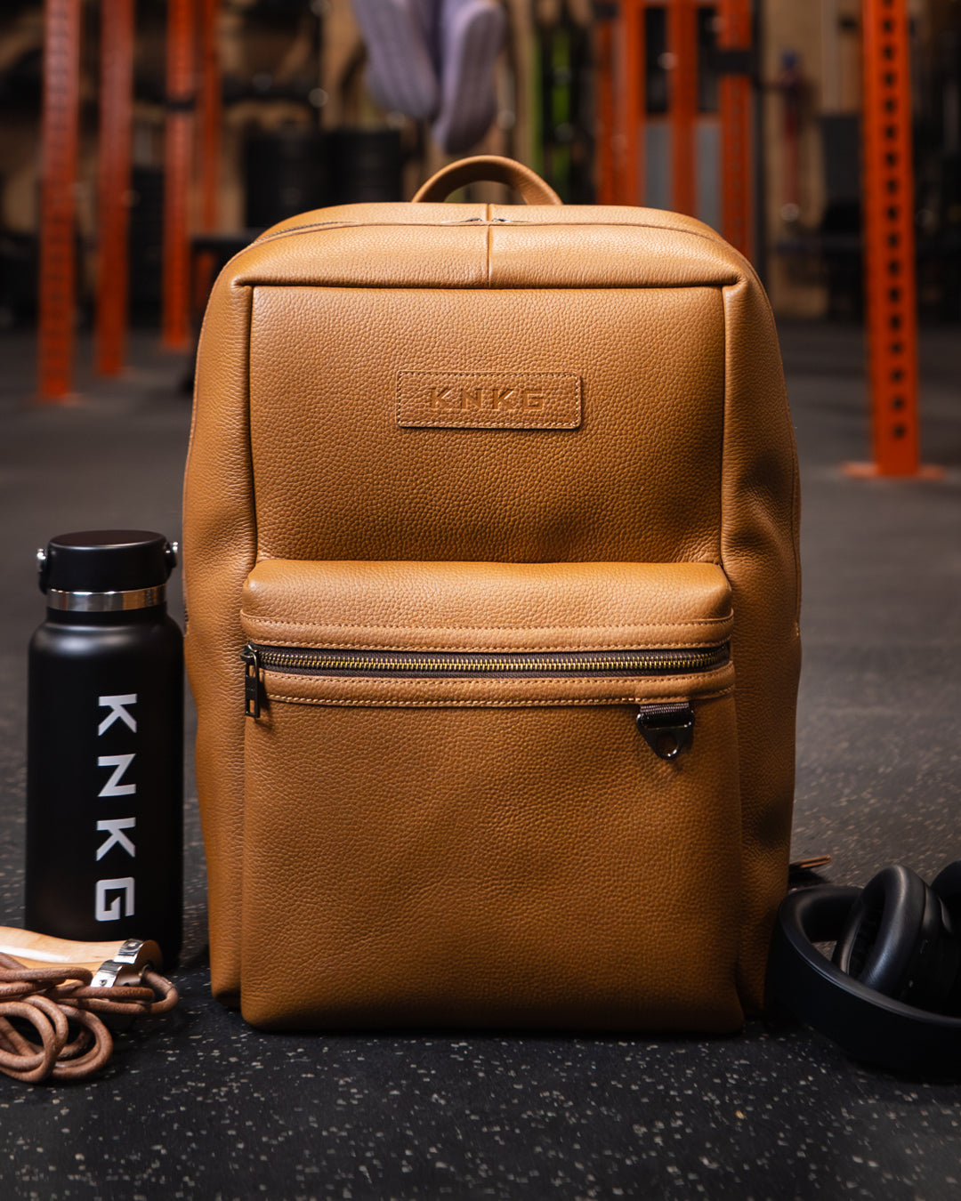 Tan leather KNKG HERITAGE Backpack sitting on gym floor next to drink bottle and leather skipping rope