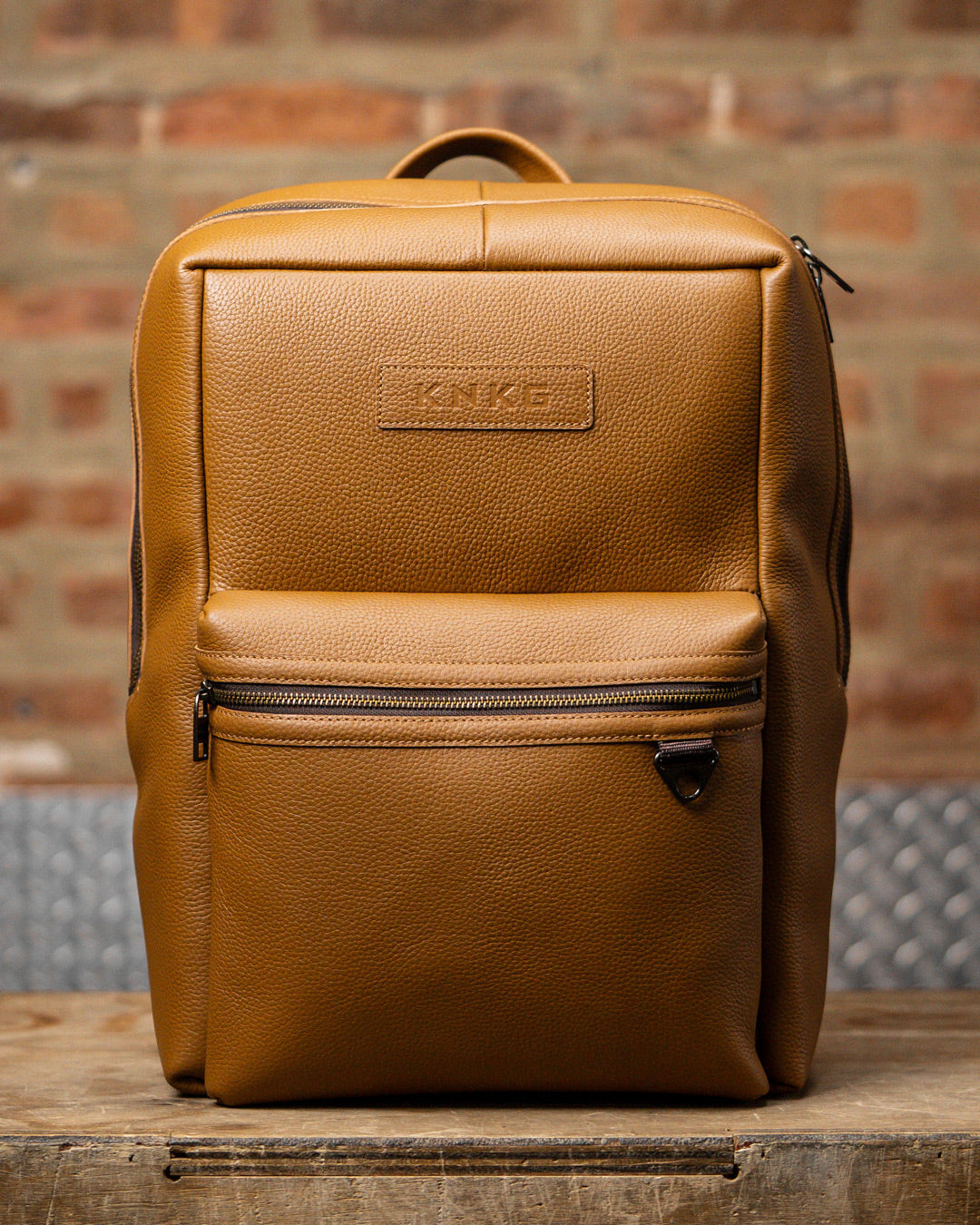 Tan leather KNKG HERITAGE Backpack sitting on wooden box inside boxing gym