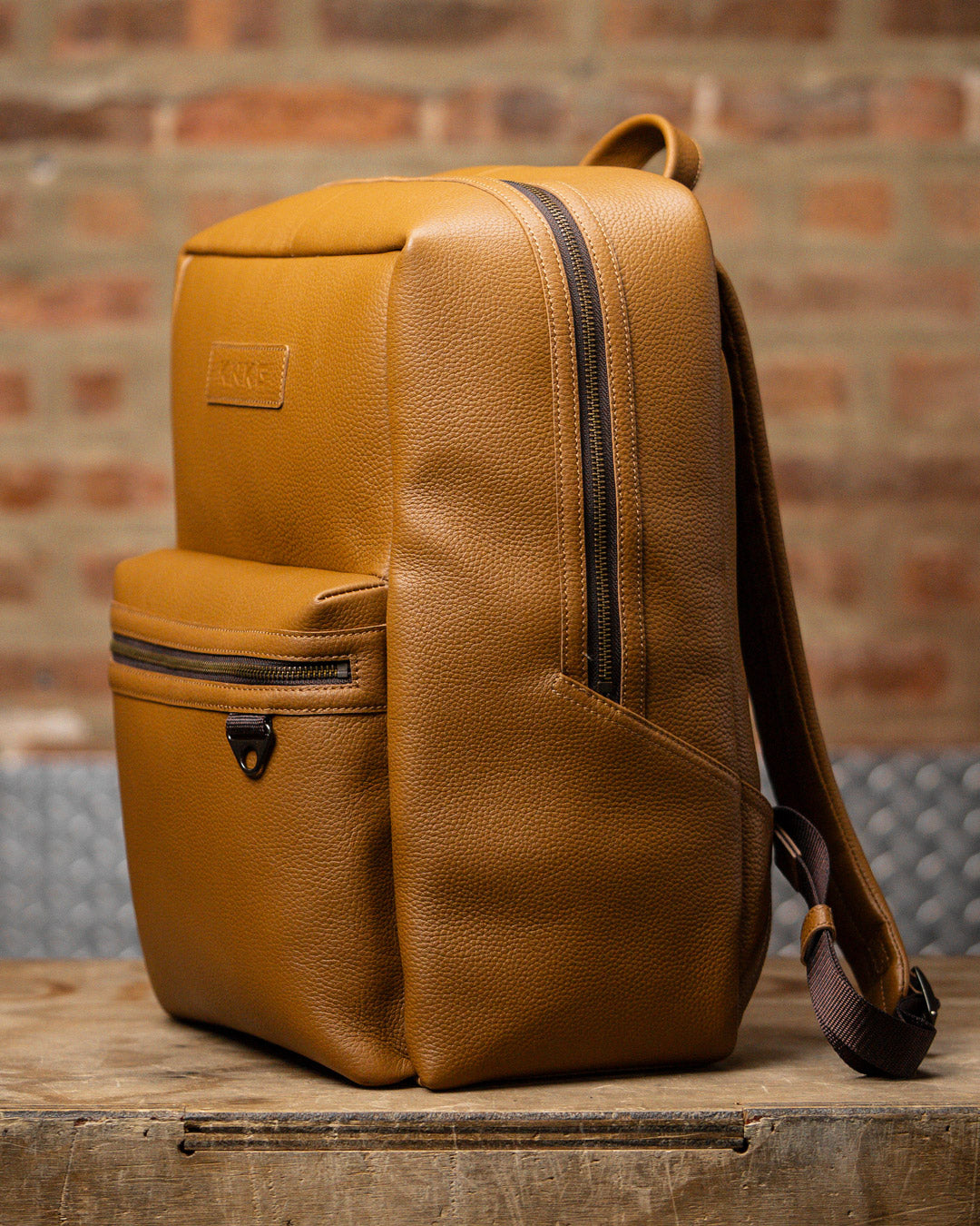 Side view of tan leather KNKG HERITAGE Backpack