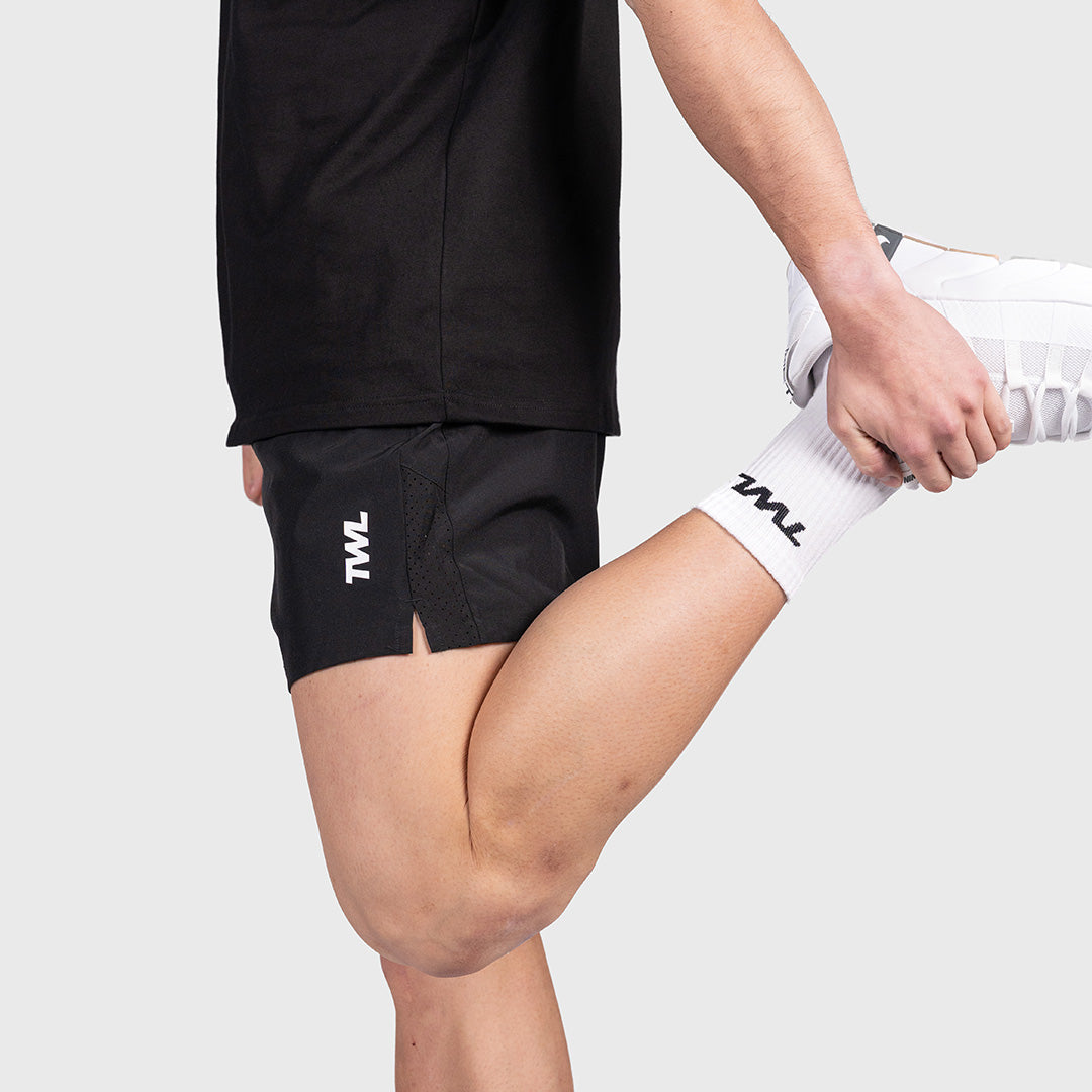 Man in the black TWL Men's Rep Shorts 5" performing a quad stretch, showing flexibility
